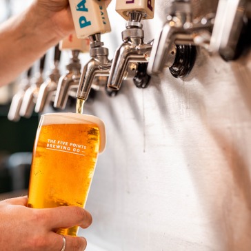 A row of silver beer taps, with a pint being filled with beer under one of them.