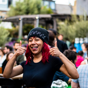 Min gives a thumbs up with both hands to the camera while in the courtyard